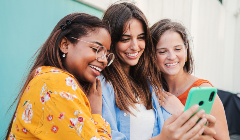 Three women smiling while looking at a green smartphone together