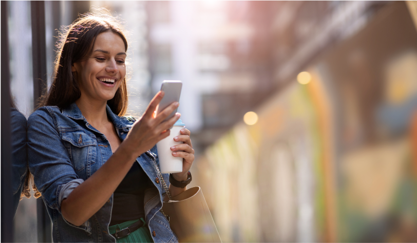 Smiling woman using smartphone while standing outside in urban setting.